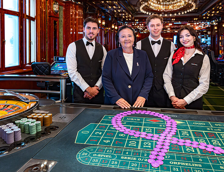 Pink Casino Night - Doris Kiefhaber Geschäftsführerin der Österr. Krebshilfe und der Aktion Pink Ribbon mit Croupière und Croupiers am Roulette-Tisch mit Pink Ribbon Symbol